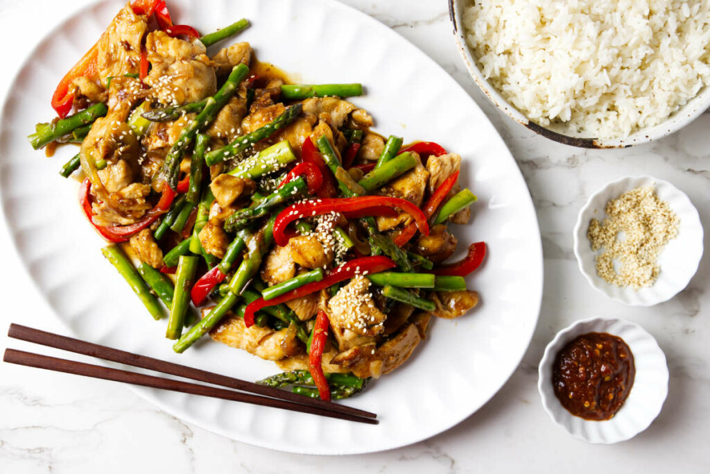 A plate filled with chicken and asparagus stir fry next to white rice.