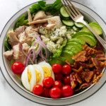 A large bowl filled with chicken cobb salad next to a fork.