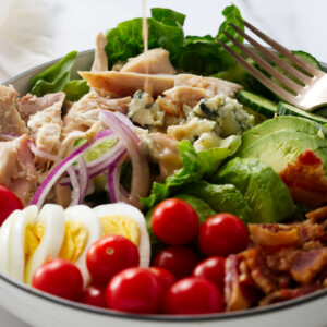 Pouring vinaigrette over a Cobb salad.