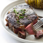 A fork picking up a bite of ribeye steak cooked in the oven.