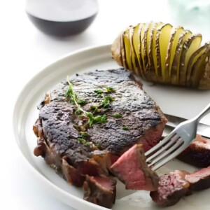 A ribeye steak on a plate next to a baked potatoe.