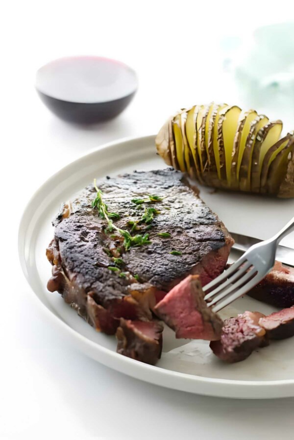 A ribeye steak on a plate next to a baked potatoe.