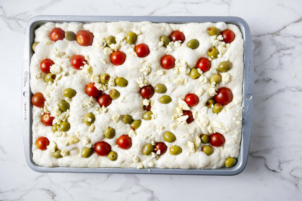 Adding tomatoes, olives, and blue cheese to focaccia bread dough.