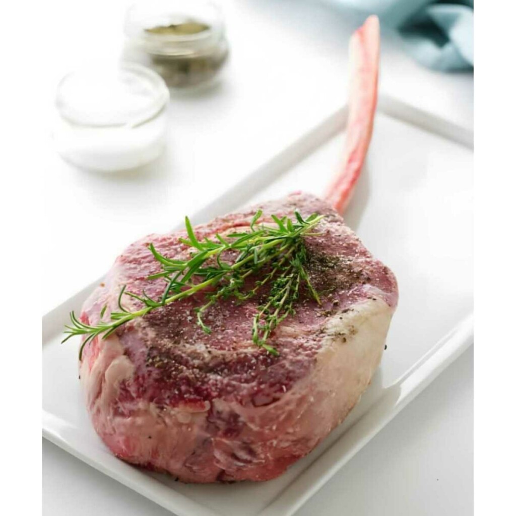 Seasoning a steak with salt, pepper and herbs.