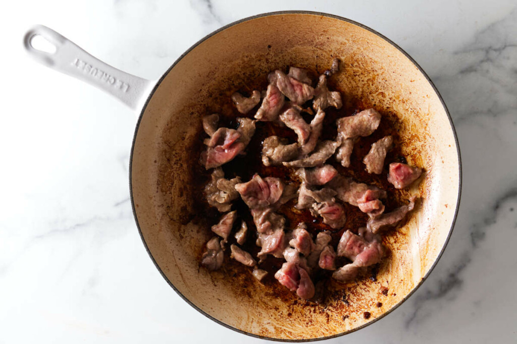 Searing strips of beef to brown them in a skillet.