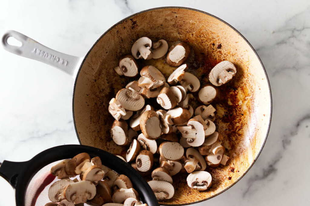 Adding sliced mushrooms to the pan.