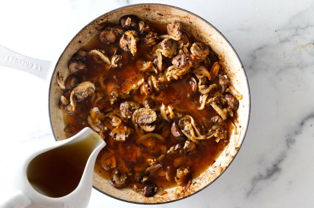 Pouring beef broth into the skillet.