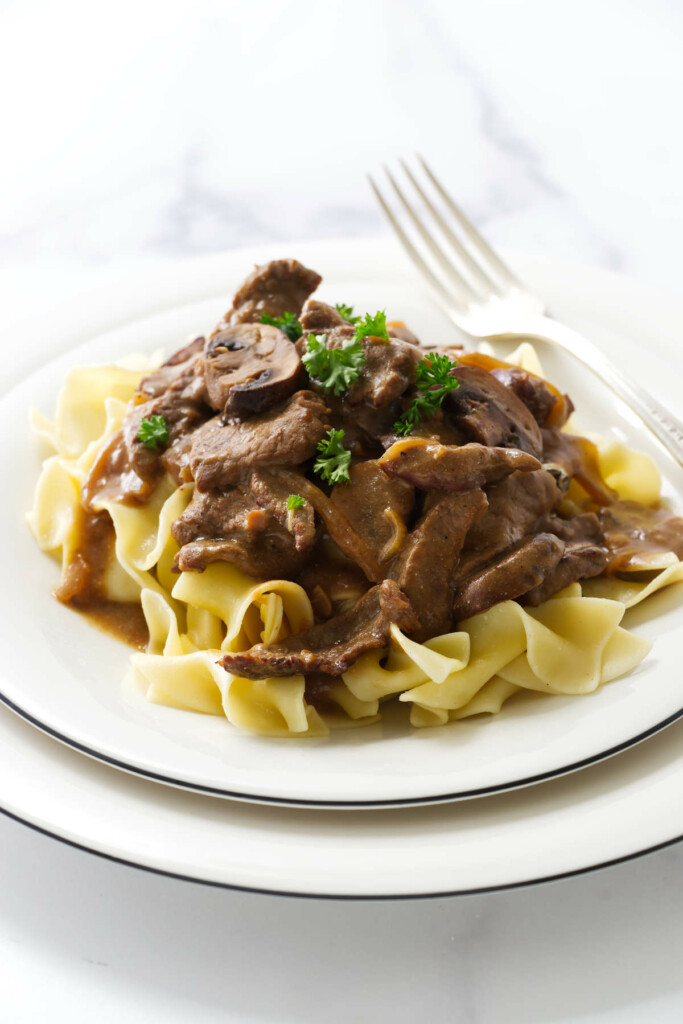Hearty beef and mushroom stroganoff spooned over a bowl of buttered noodles.