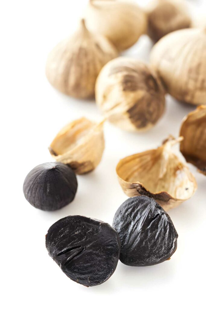 Black garlic cloves, peeled and unpeeled, arranged on a white surface.