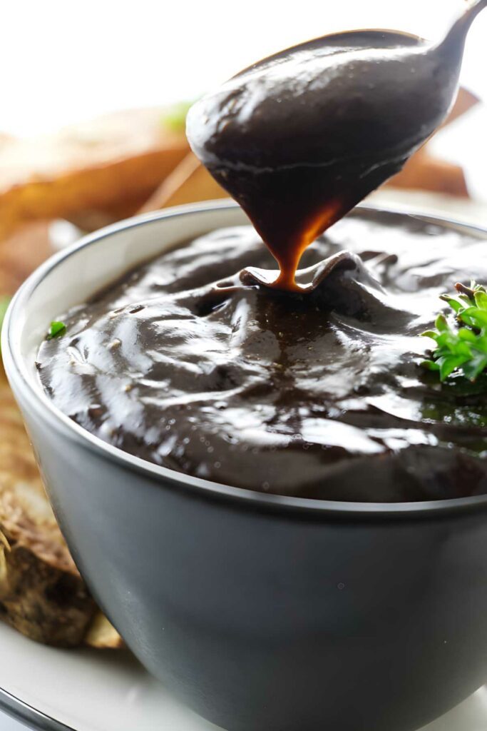 Spoon dripping black garlic mayonnaise in a bowl.
