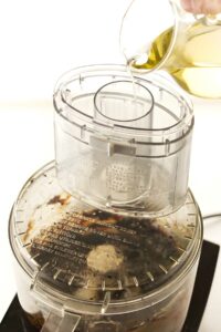 Pouring oil into a food processor while making black garlic aioli.