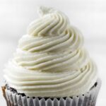 Chocolate cupcake with tall white frosting swirl in a white liner.