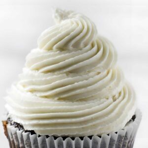 Chocolate cupcake with tall white frosting swirl in a white liner.
