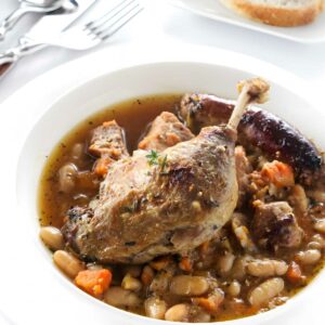 A cassoulet with duck in a bowl; bread in the background.