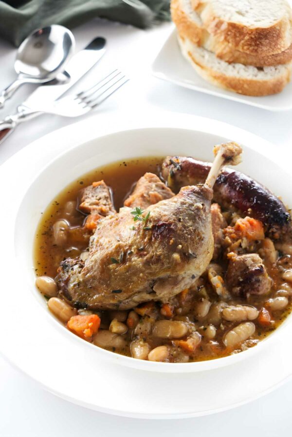A cassoulet with duck in a bowl; bread in the background.
