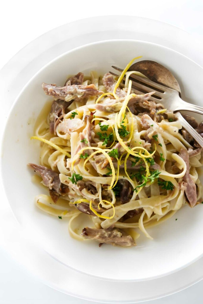 Tagliatelle pasta with shredded meat, parsley, lemon zest; fork and spoon.