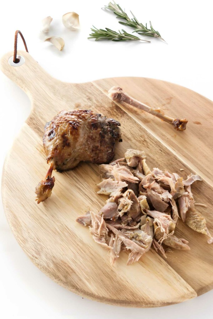 Cooked duck leg and shredded meat on cutting board.