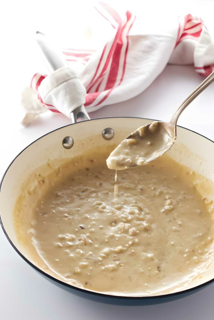 Spoon dripping creamy pepper gravy over skillet.