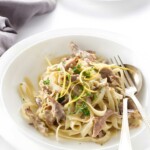 Fettuccine pasta with creamy meat sauce, salad, and utensils on table.
