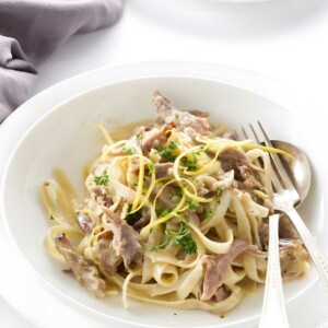 Fettuccine pasta with creamy meat sauce, salad, and utensils on table.