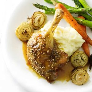 Duck leg with sauce, mashed potatoes, carrots, asparagus, and roasted onions.