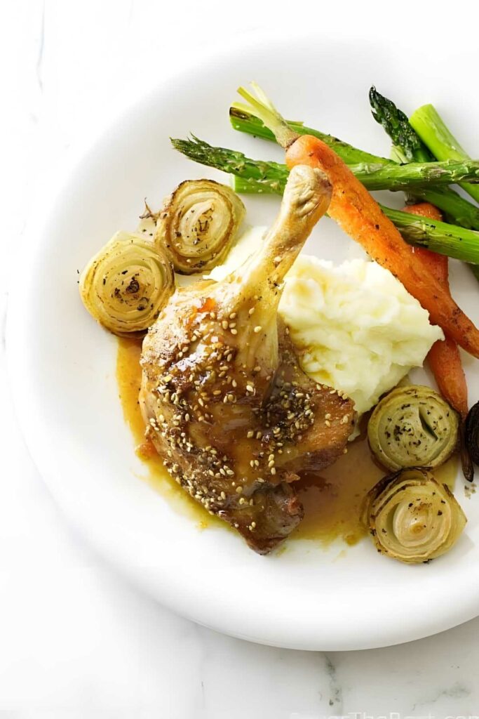 Duck leg with fig sauce, mashed potatoes, carrots, asparagus, and roasted onions.
