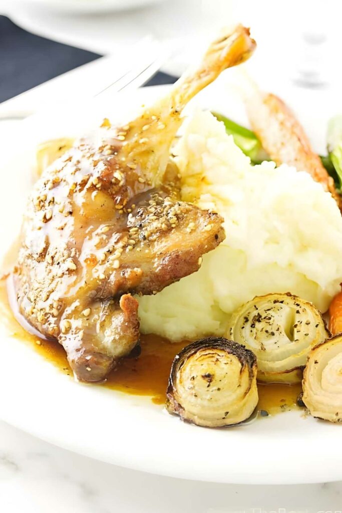 Roast duck leg with fig glaze, mashed potatoes, onions, and vegetables plated.