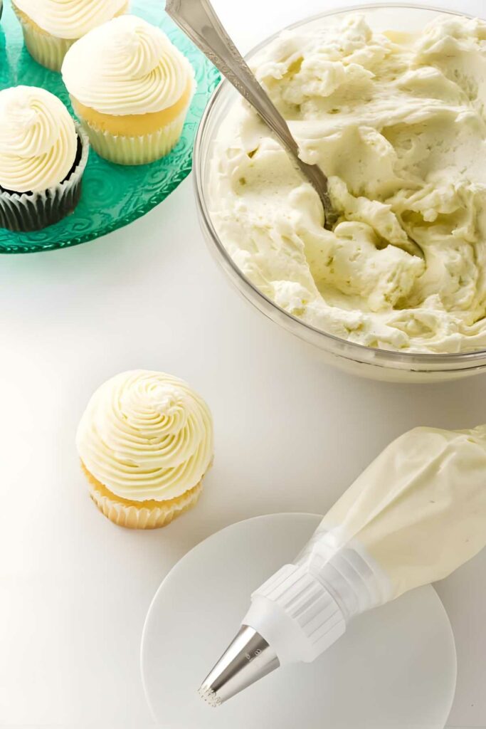 Piping bag, bowl of ermine frosting, and cupcakes.