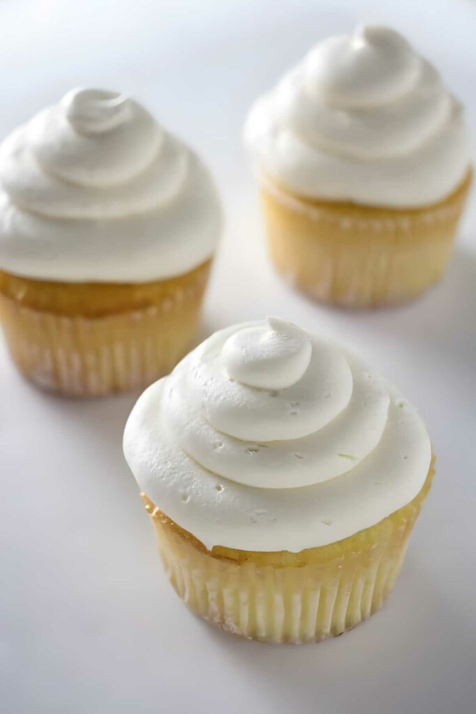 Three vanilla cupcakes with swirled vanilla buttercream frosting.