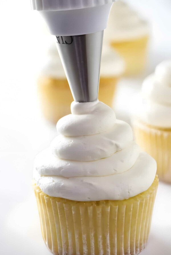 Piping bag decorating yellow cupcake with American buttercream.