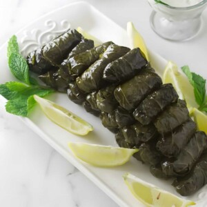 Stuffed grape leaves with lemon, mint, and sauce on a serving plate.