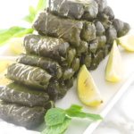 Stuffed grape leaves with rice, garnished with lemon wedges and mint.