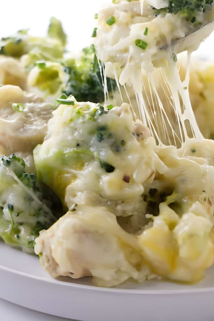 Fork lifting cheesy broccoli chicken casserole with melted cheese and chives.