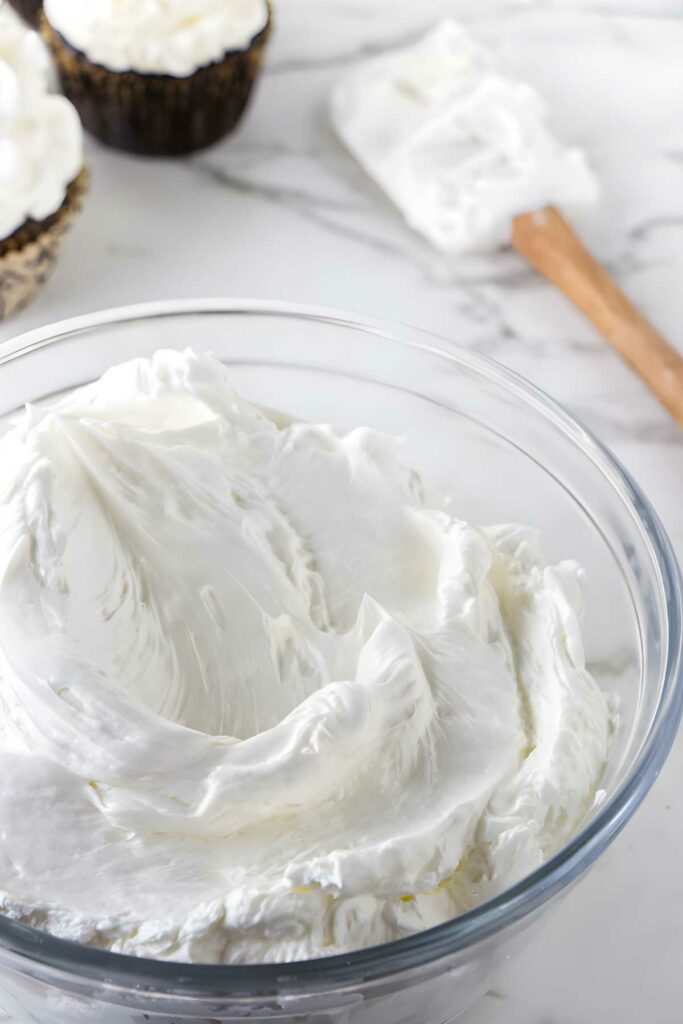 A bowl of cooked meringue buttercream in front of a spatula.