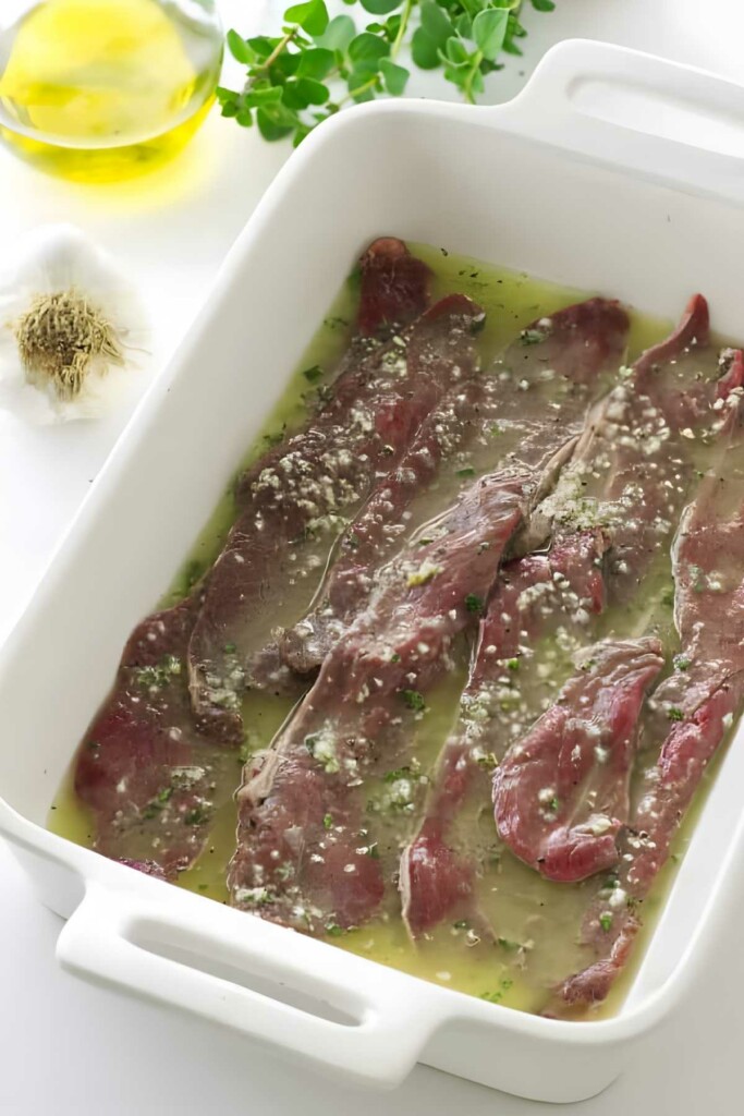 Raw beef slices marinating with herbs and garlic, olive oil nearby.