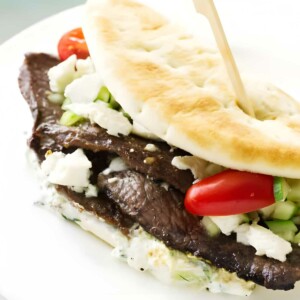 Greek flatbread sandwich with beef, feta, vegetables and creamy sauce on plate.