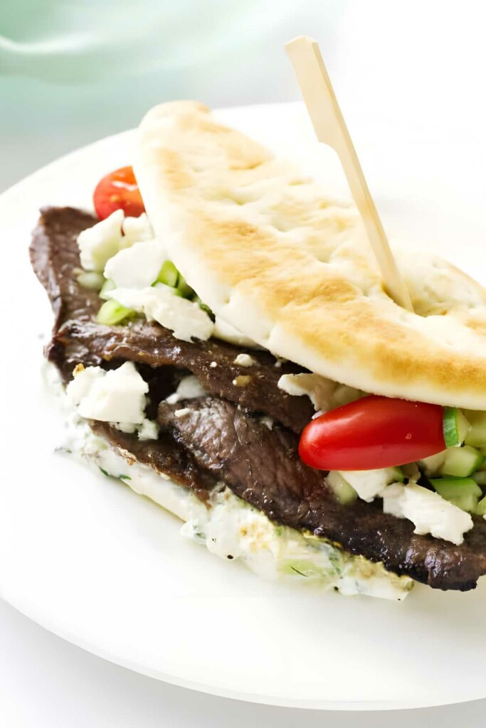 Greek flatbread sandwich with beef, feta, vegetables and creamy sauce on plate.