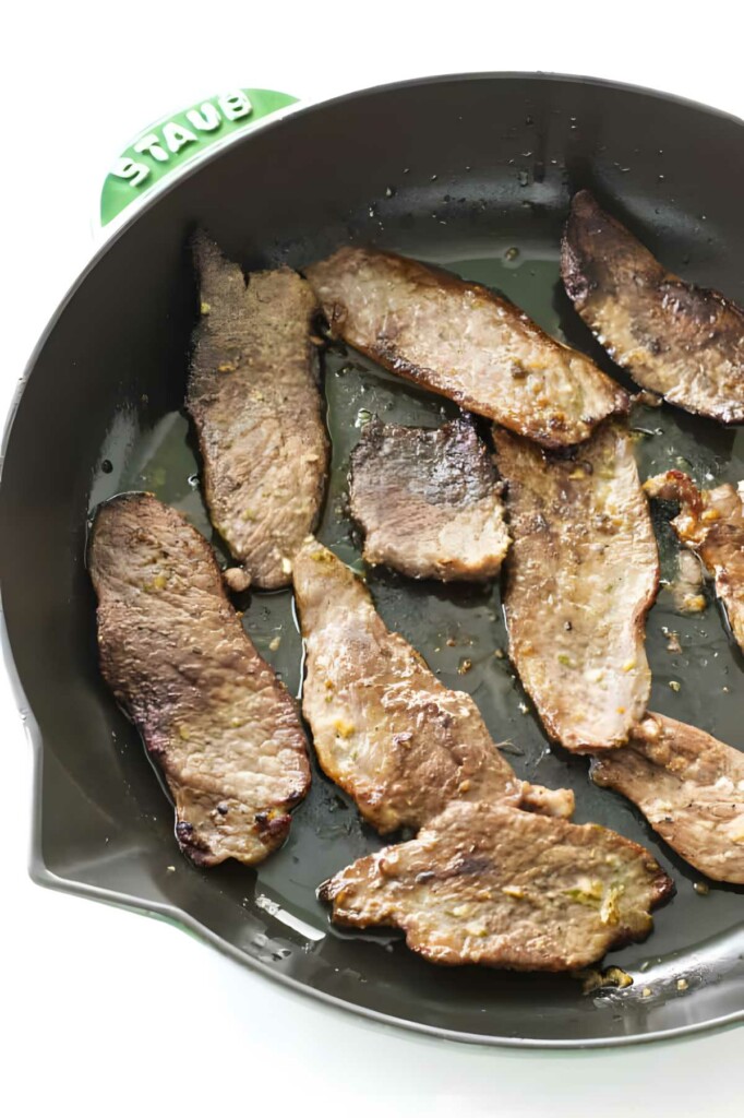 Slices of lamb cooking a a skillet for making Greek lamb sandwich.