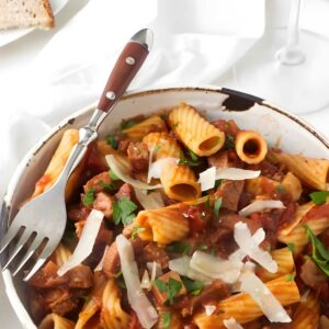 Bowl of rigatoni pasta with meat sauce, parmesan, bread, and red wine.