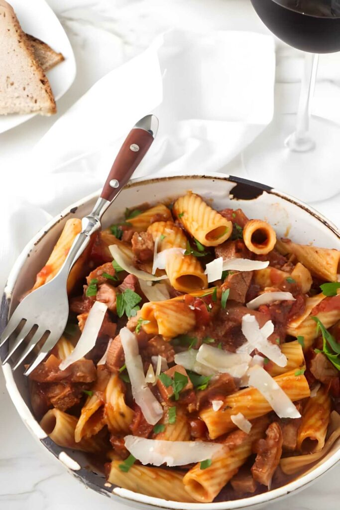 Bowl of rigatoni pasta with beef, parmesan, bread, and red wine.