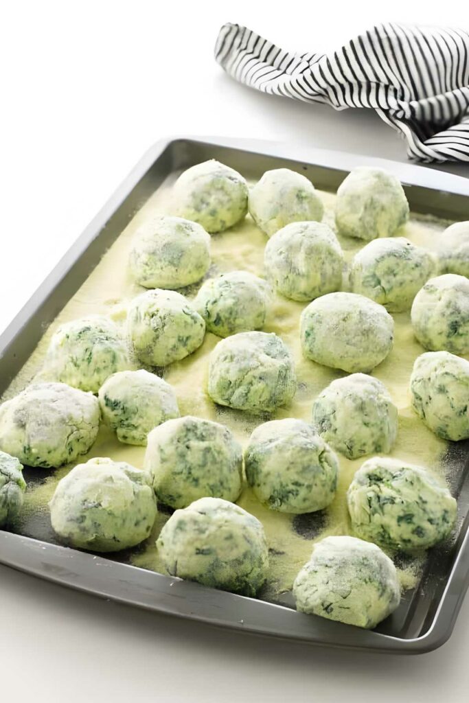 Raw spinach and ricotta dumplings on floured baking sheet.