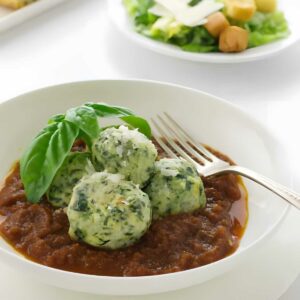 Three spinach dumplings on tomato sauce, with basil, cheese, salad, and bread.