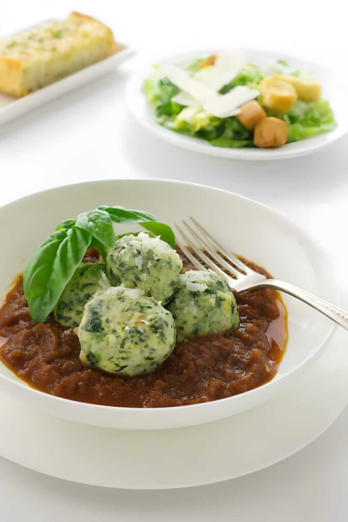 Three spinach dumplings on tomato sauce, with basil, cheese, salad, and bread.