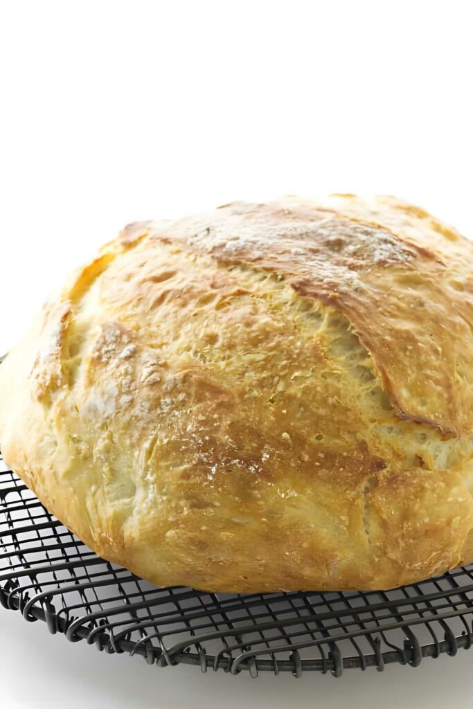 Round golden-brown loaf of bread on black wire rack, white background.