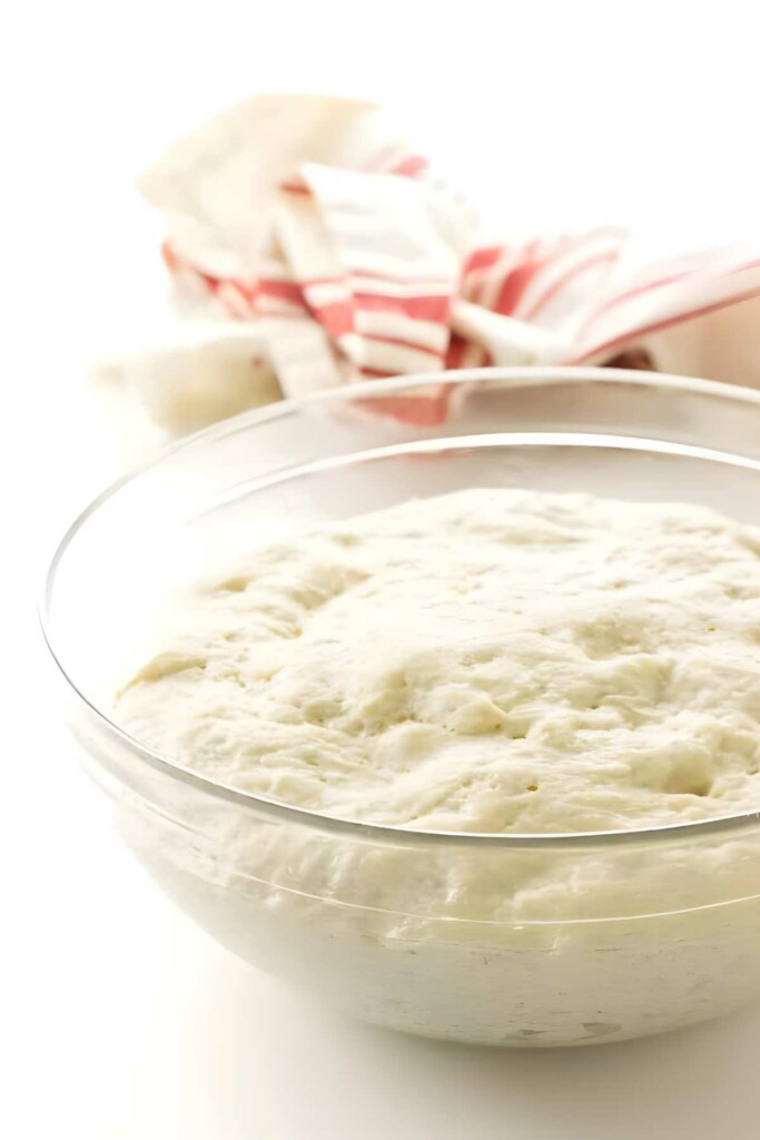Risen dough in glass bowl, red-striped cloth in background.