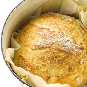 Golden-brown artisan bread loaf in a white Dutch oven.