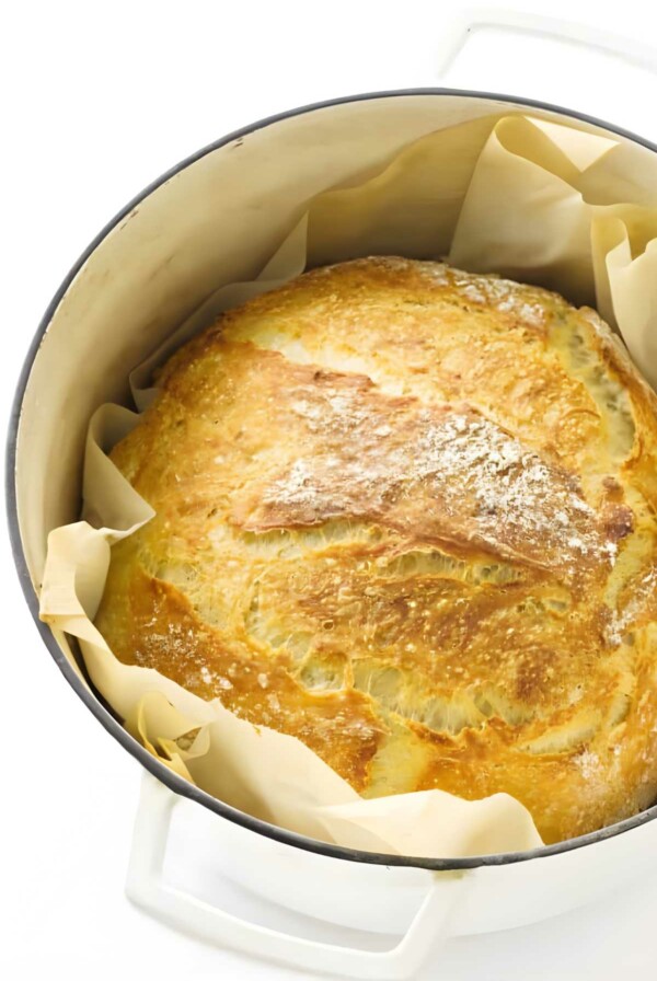 Golden-brown artisan bread loaf in a white Dutch oven.