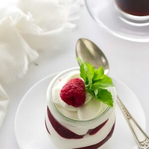 Layered dessert jar with raspberry, mint, coffee cup and spoon nearby.
