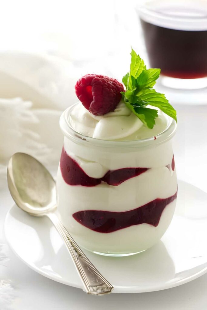 Layered yogurt parfait with berry sauce, raspberry, and mint on a plate.