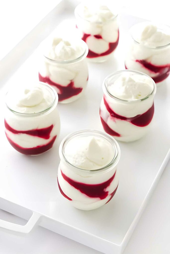 Glass jars of yogurt with red berry sauce, topped and tray-arranged.